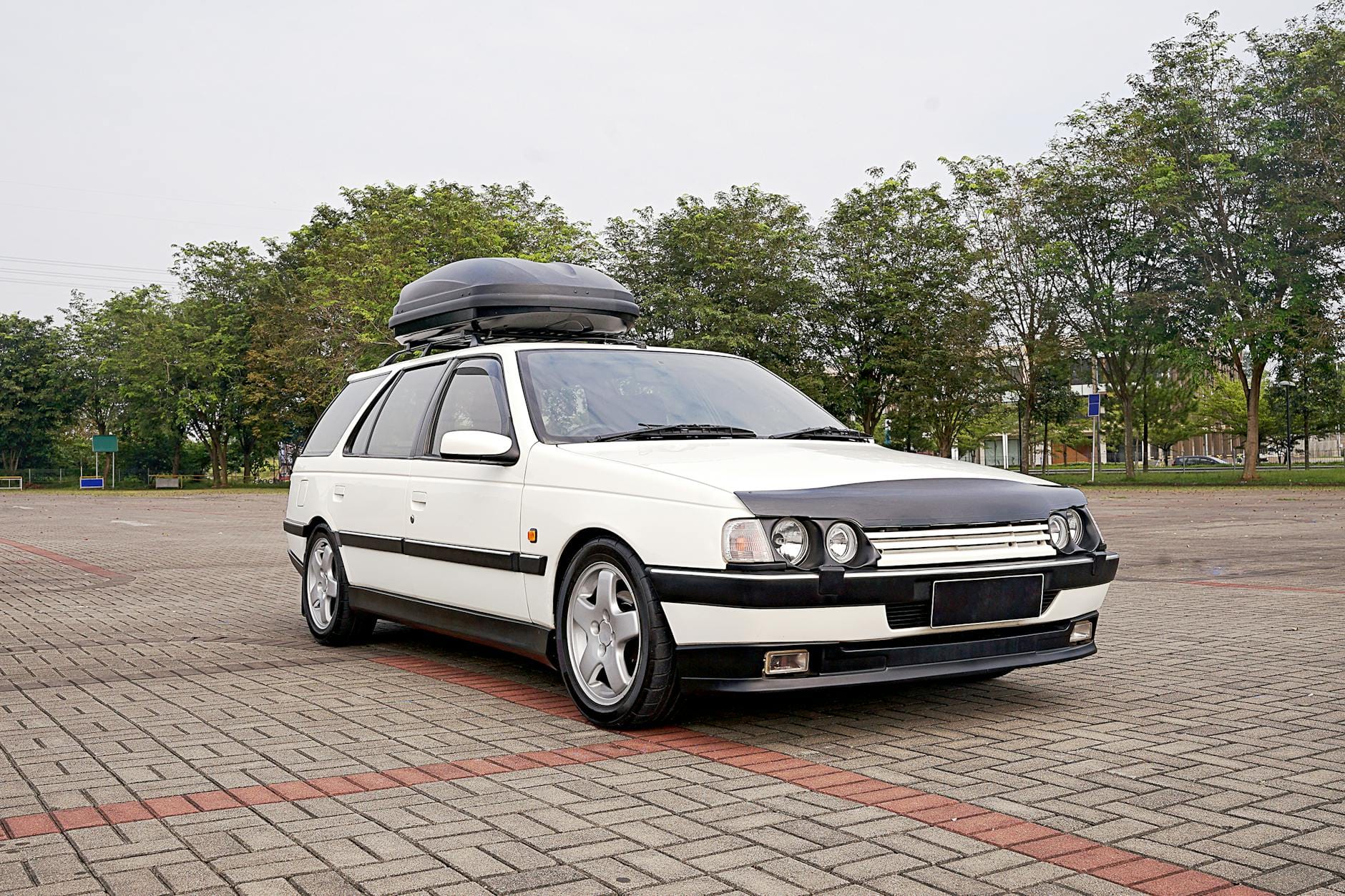 Białe kombi z wypożyczonym boksem dachowym zaparkowane w mieście